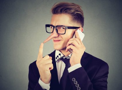 young sly man with long nose talking on mobile phone isolated on gray wall background. Liar concept. Human emotion feelings